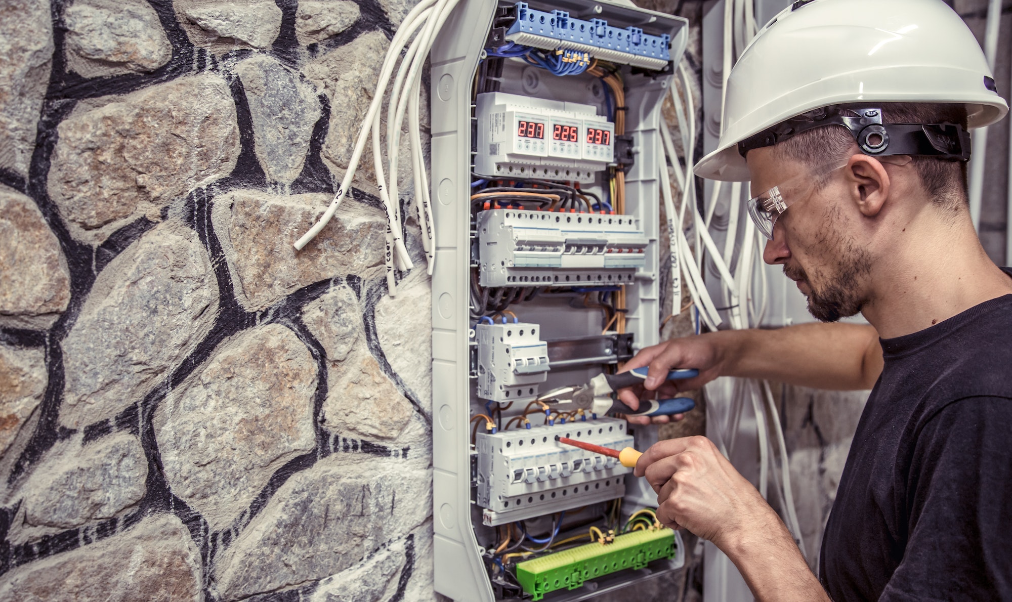 a male electrician works in a switchboard with an electrical connecting cable